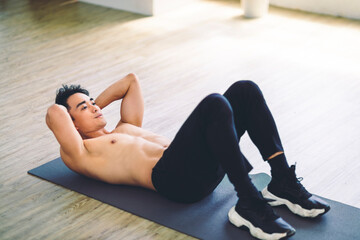 Fototapeta na wymiar Muscular Asian young man doing exercises on floor at home