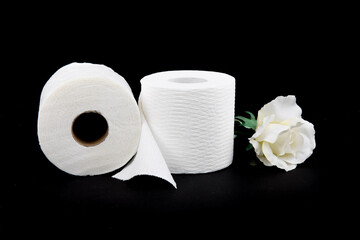 two rolls of toilet paper with a white fabric rose isolated on a black background