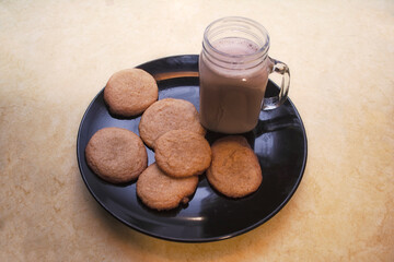 Fresh homemade cinnamon and sugar cookies on a black plate with a glass of creamy chocolate milk.