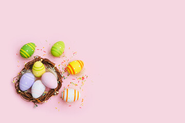 Fototapeta na wymiar Colorful easter eggs in nest on pastel pink background.