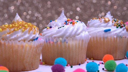 Decorated colourful cupcakes for the holiday, shallow depth of field. Close up focus on the middle muffin. Gold background. Presentation of delicious desserts at anniversary or birthday.