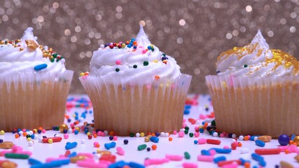 Shallow depth of field focus at middle, decorated colourful cupcakes for the holiday. Close up floating focus on the muffins. Gold background. Presentation of desserts at anniversary or birthday.