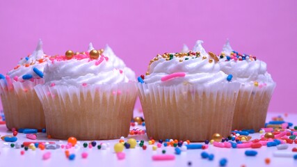Cupcakes macro shallow depth of field view. Decorated sugar sprinkles cup cakes with white vanilla cream on pink background. Delicious desserts muffins for girl birthday or Valentine day.