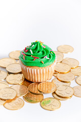Green frosted vanilla cupcake with rainbow sprinkles on a white background with gold clover coins