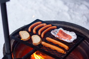 Salmon, sausages and bread on the black grill over the fire.