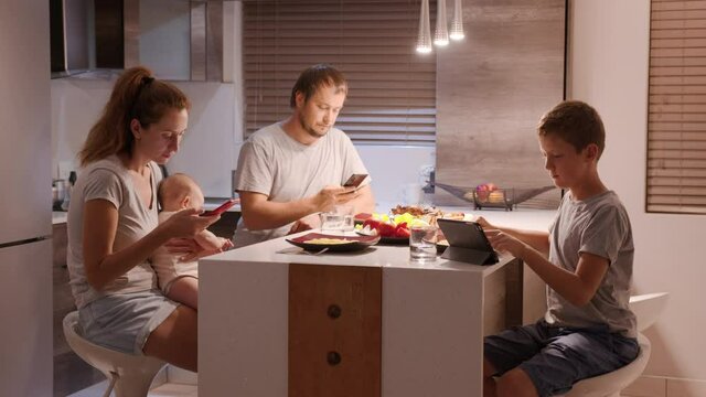 Family looking at smartphones during dinner at home.