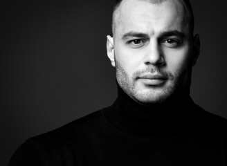 Portrait of smiling handsome brutal man in black jamper looking at camera over dark background. Stylish look for men, brutal images concept