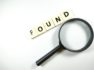 Selective focus.Magnifying glass and scrabble letters with text FOUND on white background.