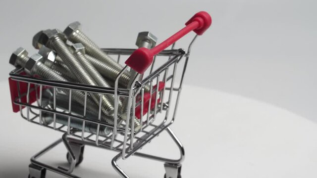a miniature shopping cart from a supermarket filled with bolts and screws rotates slowly on a white background. close detailed plan