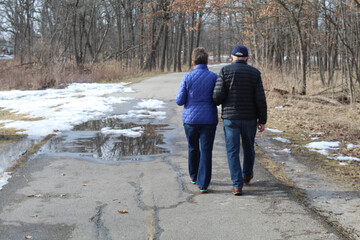 Older couple walking arm and arm at Miami Woods in Morton Grove, Illinois during a spring thaw on the North Branch Trail