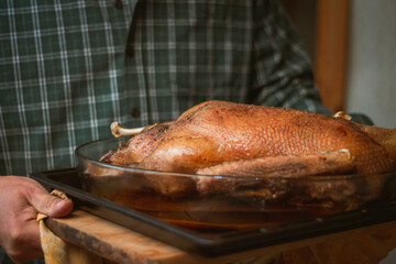 Man in green checkered shirt carries baked goose or turkey on baking sheet