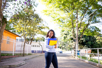 Portrait of a young college girl holding folders and notebooks and walking down the street to go to school or college. Student girl smiling and happy.