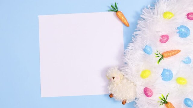 Easter eggs appear on fluffy fabric on pastel blue background with paper card note. Stop motion flat lay
