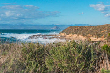 Pacific ocean, rocky cliffs, and silhouette of Morro Rock. View from Montana del Oro state park, California coastline