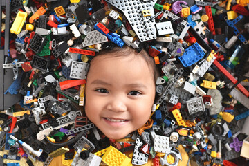 Little asian girl looking at camera surrounded by toy bricks block. Concept of Child development