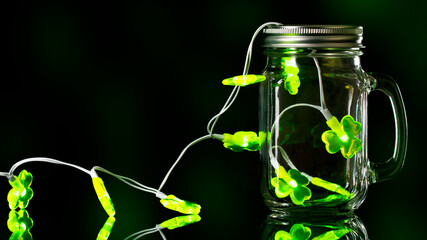St Patrick's Day. Green lights in Glass jar. Mason Jar for drinking. Empty glass jar with lid and handle on black background.