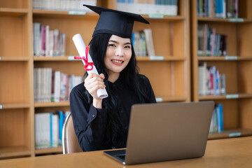 A young Asian female university graduate expressing joy and excitement to celebrate her achievement of degree graduation in front of a laptop making a remote video call to her parents at home