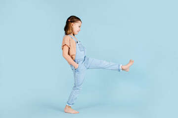 Playful little girl doing wide steps with straight legs over blue background.