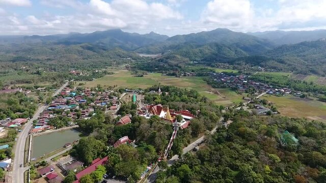 The aerial view of the village among the fields and the forest in the country that has Phra That Chohaea temple, Thai buddhist temple of Phrae province, at the middle of the village and the mountains 