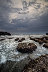 Fototapeta na wymiar Beautiful seascape for background. Beach with rocks and stones. Low tide. Motion water. Cloudy sky. Slow shutter speed. Soft focus. Copy space. Vertical layout. Mengening beach, Bali