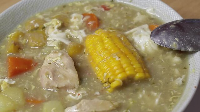 close up bowl of seasoned soup with shredded chicken, egg and corn in the center, healthy living concept at home