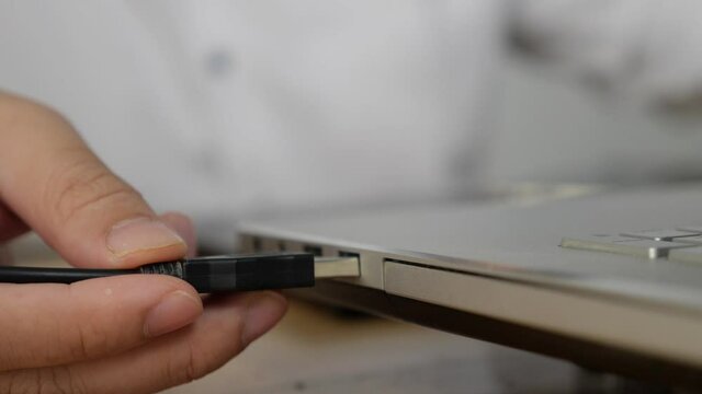 Close up of hand inserting plugging data cable into usb port in laptop; data transfer