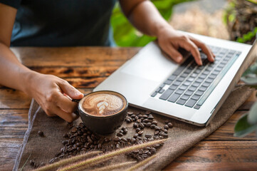 Woman holding latte art coffee cup and working with laptop computer on wood table