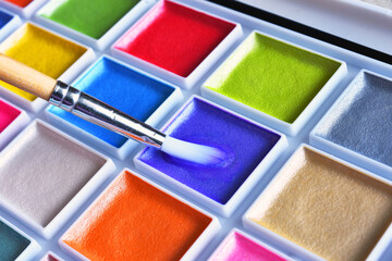 A close up image of a brightly colored set of water color paints with paint brushes.  