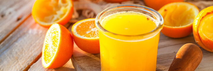Glass of freshly sqeezed orange juice on a wooden table. Natural source of vitamins, healthy beverage for ideal breakfast. Bright sunny summer day. Close up, copy space for text. Banner