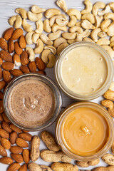 The modern concept of wellness and veganism. Jars of almond, cashew and peanut butter on a white wooden table. Organic, homemade nut butter for a healthy breakfast.
