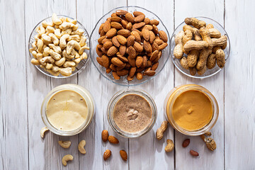 The modern concept of wellness and veganism. Jars of almond, cashew and peanut butter on a white wooden table. Organic, homemade nut butter for a healthy breakfast.