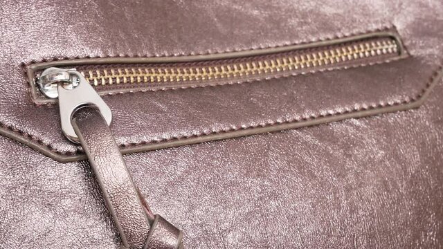 Close-up of a zipper on the side pocket of a leather bag and a man's hand fastening it
