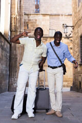 Fototapeta na wymiar Portrait of smiling happy friends tourists with luggage on the street of old european city