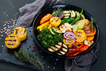 Grilled assorted vegetables in cast iron pan on black background.