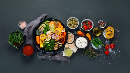 Grilled assorted vegetables in cast iron pan on black background.