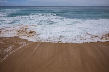 Seascape background. Sandy beach, milky foam waves, blue ocean. Scenic waterscape. Horizon line. Nature and environment concept. Daylight. Copy space. Dreamland beach, Bali