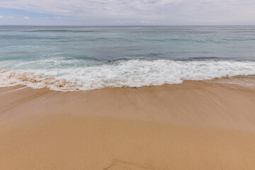 Fototapeta na wymiar Seascape background. Sandy beach, milky foam waves, blue ocean. Scenic waterscape. Horizon line. Nature and environment concept. Daylight. Copy space. Dreamland beach, Bali