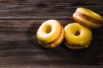 bright three yellow donuts with banana filling on a wooden table, delicious breakfast, place for text