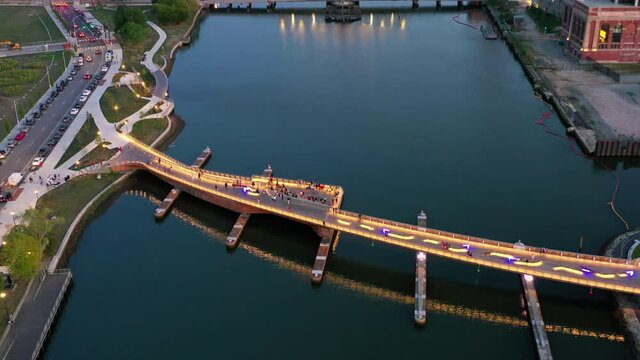 Aerial tilt down shot of people on bridge over river in city at sunset, drone flying over structures - Providence, Rhode Island