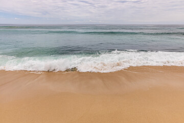 Fototapeta na wymiar Seascape background. Sandy beach, milky foam waves, blue ocean. Scenic waterscape. Horizon line. Cloudy sky. Nature and environment concept. Daylight. Copy space. Dreamland beach, Bali