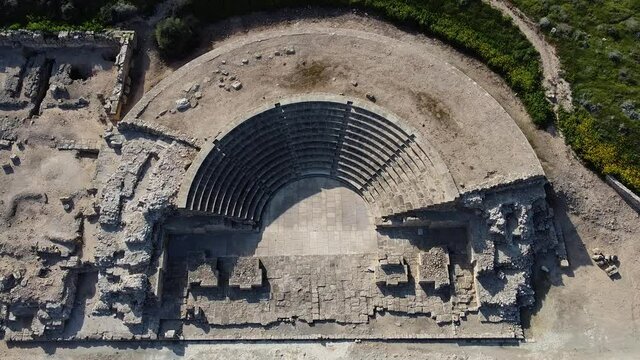 Wide aerial view of an ancient Greek Odeon, amphitheater. Top-down rising view showing the entire half-circle ruins.