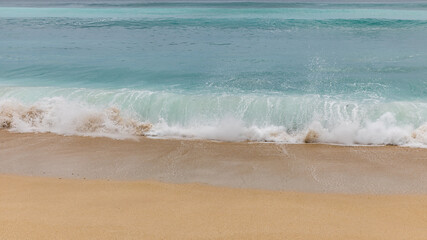 Fototapeta na wymiar Seascape background. Sandy beach, milky foam waves, blue ocean. Scenic waterscape. Nature and environment concept. Daylight. Copy space. Dreamland beach, Bali