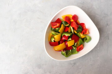 Fresh raw yellow, green, red bell peppers, and onions placed in a white bowl. Diced colorful...