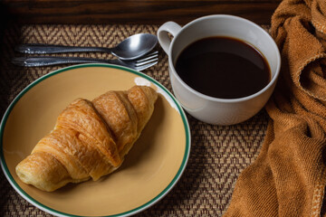 Croissant and black coffee cup on dark background.