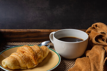 Croissant and black coffee cup on dark background.