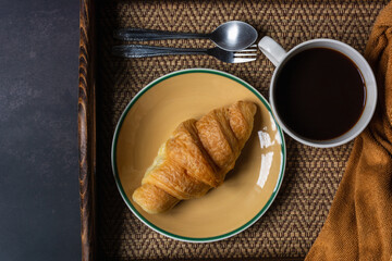 Croissant and black coffee cup on dark background.