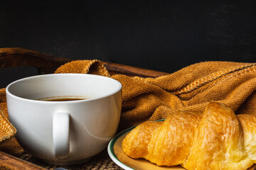 Croissant and black coffee cup on dark background.