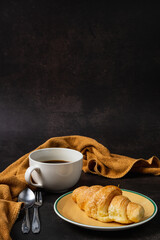 Croissant and black coffee cup on dark background.
