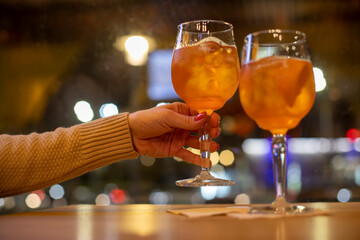 Close up view of woman hands holding glass with cocktail of orange color. one more glass is standing on table