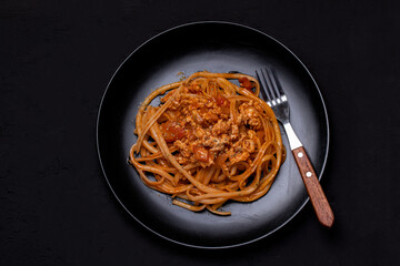 Spaghetti Sautéed Tomato Sauce with Chicken in a Black Plate on a Black Table